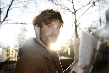 Portrait of young man with newspaper at backlight - FMKF002238