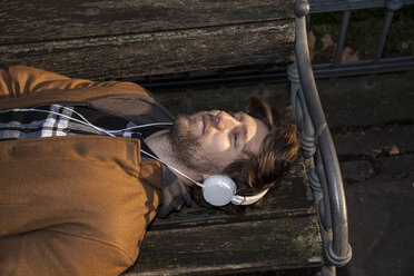 Portrait of young man lying on a bench hearing music with headphones - FMKF002239