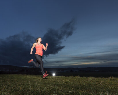 Junge Frau joggt bei Sonnenuntergang auf einer Wiese - STSF000991