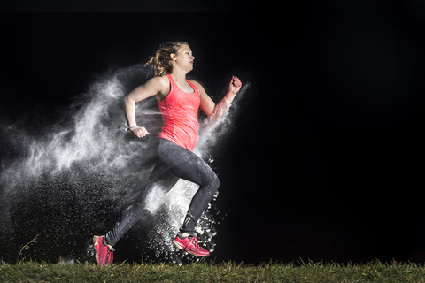 Junge Frau joggt in einer Staubwolke vor einem schwarzen Hintergrund, lizenzfreies Stockfoto