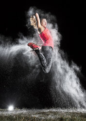 Junge Frau springt in die Luft in einer Staubwolke vor schwarzem Hintergrund - STSF000994