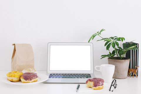 Stilleben mit Laptop, Donuts und Pflanze auf dem Schreibtisch, lizenzfreies Stockfoto