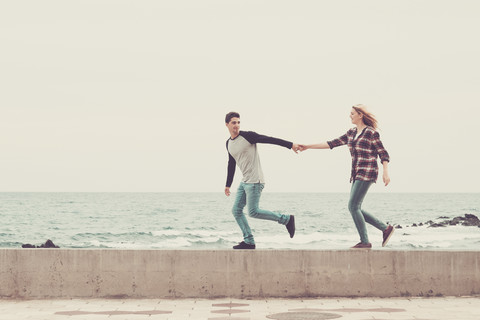 Junges Paar spaziert Hand in Hand am Meer, lizenzfreies Stockfoto