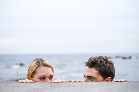 Verspieltes junges Paar, das sich hinter einer Mauer ansieht, lizenzfreies Stockfoto