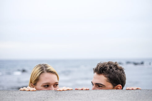 Playful young couple looking at each other behind a wall - SIPF000028