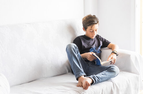 Junge sitzt auf einer weißen Couch und liest ein Buch - SIPF000035