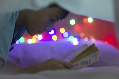 Junge liest Buch unter einer Decke, lizenzfreies Stockfoto