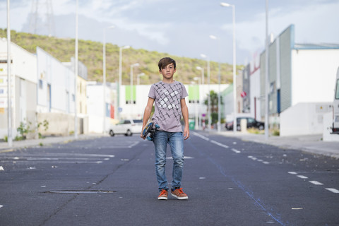 Spanien, Teneriffa, Porträt eines Jungen, der mit seinem Skateboard auf einer Straße steht, lizenzfreies Stockfoto