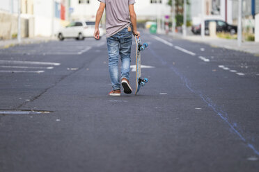 Rückenansicht eines Jungen, der sein Skateboard auf einer Straße trägt - SIPF000042