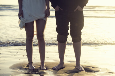 Spain, Cadiz, legs of young couple standing barefoot atseafront - KIJF000109