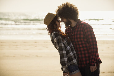 Spain, Cadiz, young couple in love standing face to face on the beach - KIJF000110