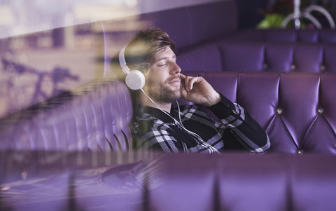 Junger Mann sitzt in einer Lounge-Bar und hört Musik mit Kopfhörern, lizenzfreies Stockfoto