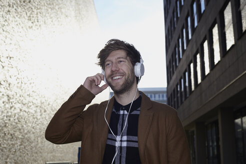 Lächelnder junger Mann hört Musik mit Kopfhörern bei Gegenlicht - FMKF002246