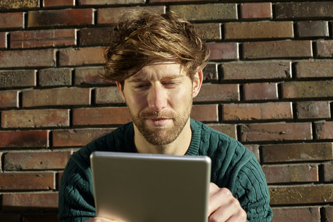 Porträt eines jungen Mannes mit digitalem Tablet vor einer Backsteinmauer, lizenzfreies Stockfoto