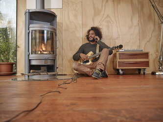 Young man with electric guitar at the fireplace talking on cell phone - RHF001220