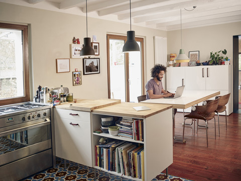 Junger Mann mit Laptop in offener Küche, lizenzfreies Stockfoto
