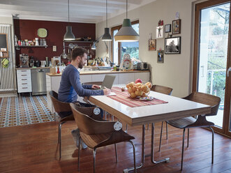 Young man using laptop in open plan kitchen - RHF001249