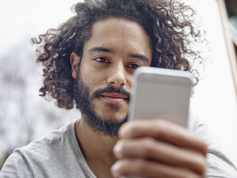 Junger Mann schaut auf sein Handy, lizenzfreies Stockfoto