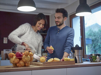 Couple in kitchen slicing oranges for freshly squeezed orange juice - RHF001264