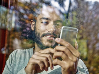 Young man using cell phone behind windowpane - RHF001267