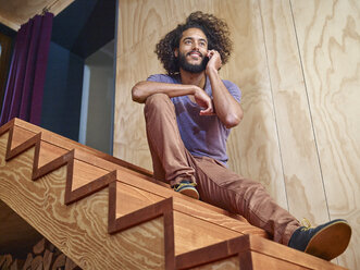 Junger Mann auf Holztreppe spricht mit Handy - RHF001272