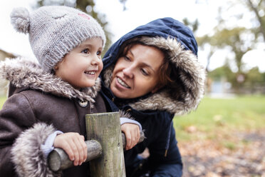 Porträt eines glücklichen kleinen Mädchens mit ihrer Mutter auf einem Spielplatz im Herbst - MGOF001244