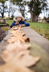 Porträt eines kleinen Mädchens, das mit Herbstblättern im Park spielt - MGOF001248