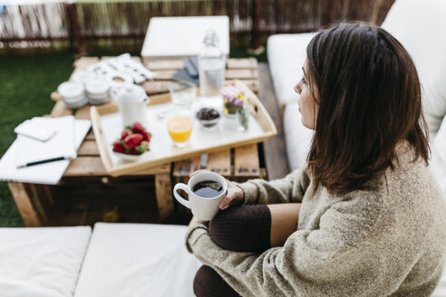 Nachdenkliche Frau sitzt mit einer Tasse Tee auf dem Balkon - JRFF000287