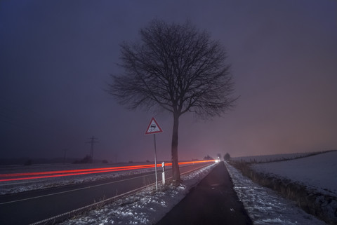 Deutschland, Niedersachsen, dribbelnde Autos auf der Straße, Nebel am Abend, Langzeitbelichtung, lizenzfreies Stockfoto