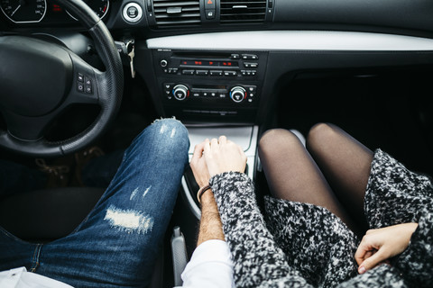 Junges Paar fährt im Auto und hält Händchen, lizenzfreies Stockfoto