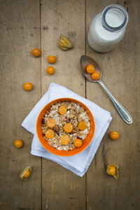 Schale mit Müsli und Physalis, Milchflasche auf Holz - LVF004391