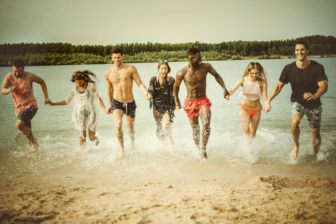 Deutschland, Haltern, sieben Freunde laufen Hand in Hand aus dem Silbersee und haben Spaß, lizenzfreies Stockfoto