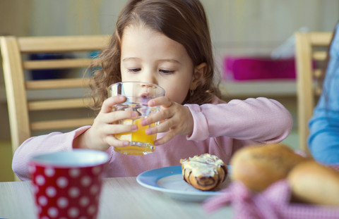 Porträt eines kleinen Mädchens, das am Frühstückstisch ein Glas Orangensaft trinkt, lizenzfreies Stockfoto