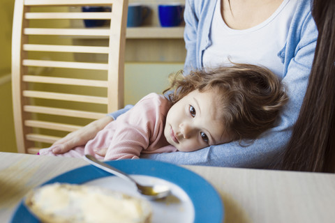 Porträt eines kleinen Mädchens in den Armen ihrer Mutter am Frühstückstisch, lizenzfreies Stockfoto