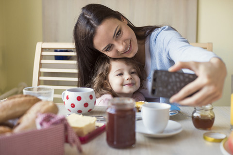 Porträt einer Mutter und ihrer kleinen Tochter, die ein Selfie am Frühstückstisch machen, lizenzfreies Stockfoto