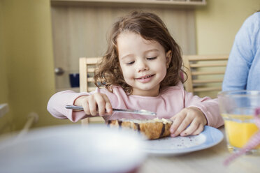 Porträt eines lächelnden kleinen Mädchens, das Butter auf ihr Croissant streicht - HAPF000126