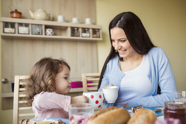 Mother and her little daughter toasting with their cups at breakfast table - HAPF000128