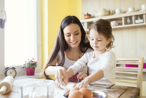 Porträt eines kleinen Mädchens und ihrer Mutter, die gemeinsam am Küchentisch Teig ausrollen - HAPF000140