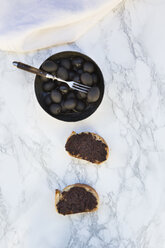 Schale mit schwarzen Oliven und zwei Scheiben Weißbrot mit Olivenpaste auf Marmor - LVF004408