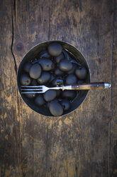 Schale mit schwarzen Oliven und Gabel auf dunklem Holz - LVF004409