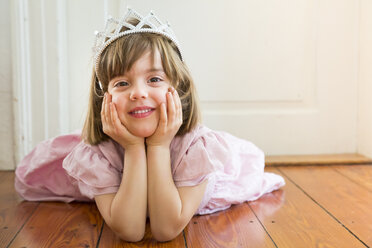 Portrait of smiling little girl dressed up as a princess lying on wooden floor - LVF004414