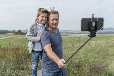Germany, Rhineland-Palatinate, portrait of father and little son taking a photo with selfie stick in nature - PAF001526