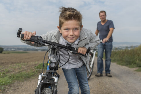 Porträt eines kleinen Jungen auf Fahrradtour mit seinem Vater im Hintergrund - PAF001528