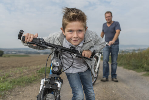 Portrait of little boy on bicycle tour with his father in the background - PAF001528