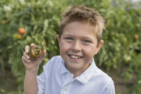 Porträt eines kleinen Jungen, der eine Tomate mit fehlendem Biss hält - PAF001531