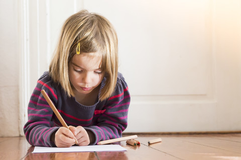 Little girl lying on the floor drawing something stock photo