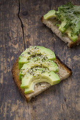 Slice of toasted bread with acocado, cress and hemp seeds on wood - LVF004425