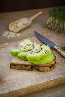 Halbe Scheibe getoastetes Brot mit Acocado und Hanfsamen auf Holzbrett - LVF004436