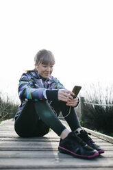 Junge Frau entspannt sich nach dem Laufen und benutzt ihr Smartphone - JRFF000337