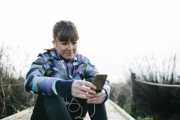 Junge Frau entspannt sich nach dem Laufen und benutzt ihr Smartphone - JRFF000338